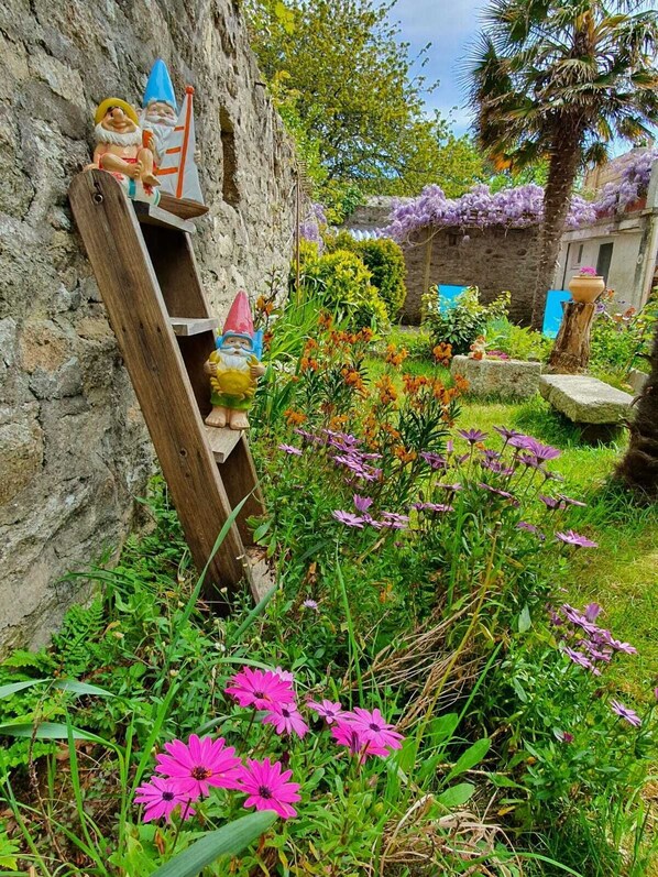 A rustic garden with stone walls, wooden structures, and vibrant flowers.