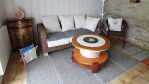 A cozy room with a wicker sofa, a round wooden table, and a stone wall. - Maison typique pour 4 personnes, jardin clos et fleuri, proche plage (Treffiagat)