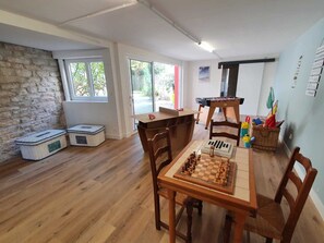 A cozy room with a wooden table set for a game, a foosball table, and a window with a view of greenery.