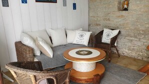 A cozy seating area with wicker furniture, a round table with a rope centerpiece, and a stone wall. - Maison typique pour 4 personnes, jardin clos et fleuri, proche plage (Treffiagat)