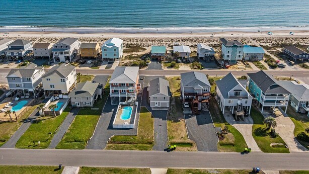 A coastal residential area with houses, a swimming pool, and a beach in the background. - Heart of Oak Island/2nd Row Ocean Vew - 3 Bedrooms (Oak Island)