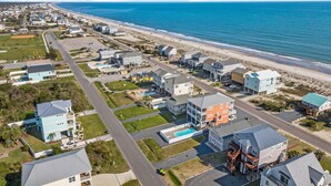 An aerial view of a coastal residential area with houses, a beach, and a clear blue sky. - Heart of Oak Island/2nd Row Ocean Vew - 3 Bedrooms (Oak Island)