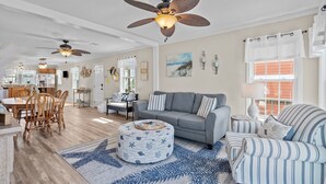 A spacious living area with a gray sofa, striped armchairs, a round ottoman, and a ceiling fan. - Heart of Oak Island/2nd Row Ocean Vew - 3 Bedrooms (Oak Island)
