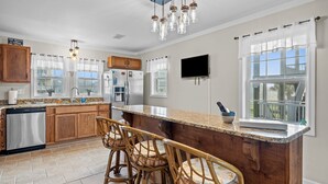 A kitchen with wooden cabinets, a granite countertop, a built-in dishwasher, and a large island with bar stools. - Heart of Oak Island/2nd Row Ocean Vew - 3 Bedrooms (Oak Island)