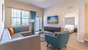 A modern living room with a sofa, armchair, and a dining table. There is a bed with a headboard and a TV mounted on the wall. - 4012 Vista Cay (Orlando)
