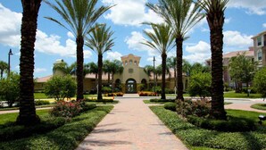 A pathway leading to a building with a central entrance, flanked by palm trees and well-maintained gardens. - 4012 Vista Cay (Orlando)