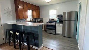 A modern kitchen with wooden cabinets, a central island with bar stools, a stainless steel refrigerator, and a built-in oven. - Moonlight on the White- Fayetteville river cabin (Springdale)