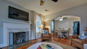 A living room with a fireplace, a dining area, and a kitchen in the background. - Bama Bungalow - Book for football season and more! (Tuscaloosa)
