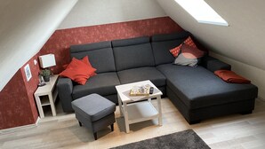 Quarto de estilo loft moderno com um sofá seccional cinza, uma pequena mesa lateral branca, um banquinho cinza e uma mesa de centro branca.