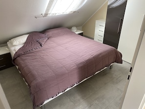A bedroom with a bed, a nightstand, a dresser, and a window with curtains.