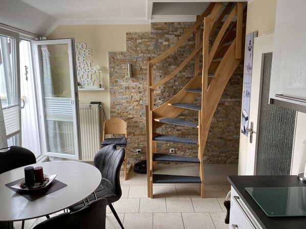 A modern kitchen with a built-in oven, a wooden staircase, and a stone wall.