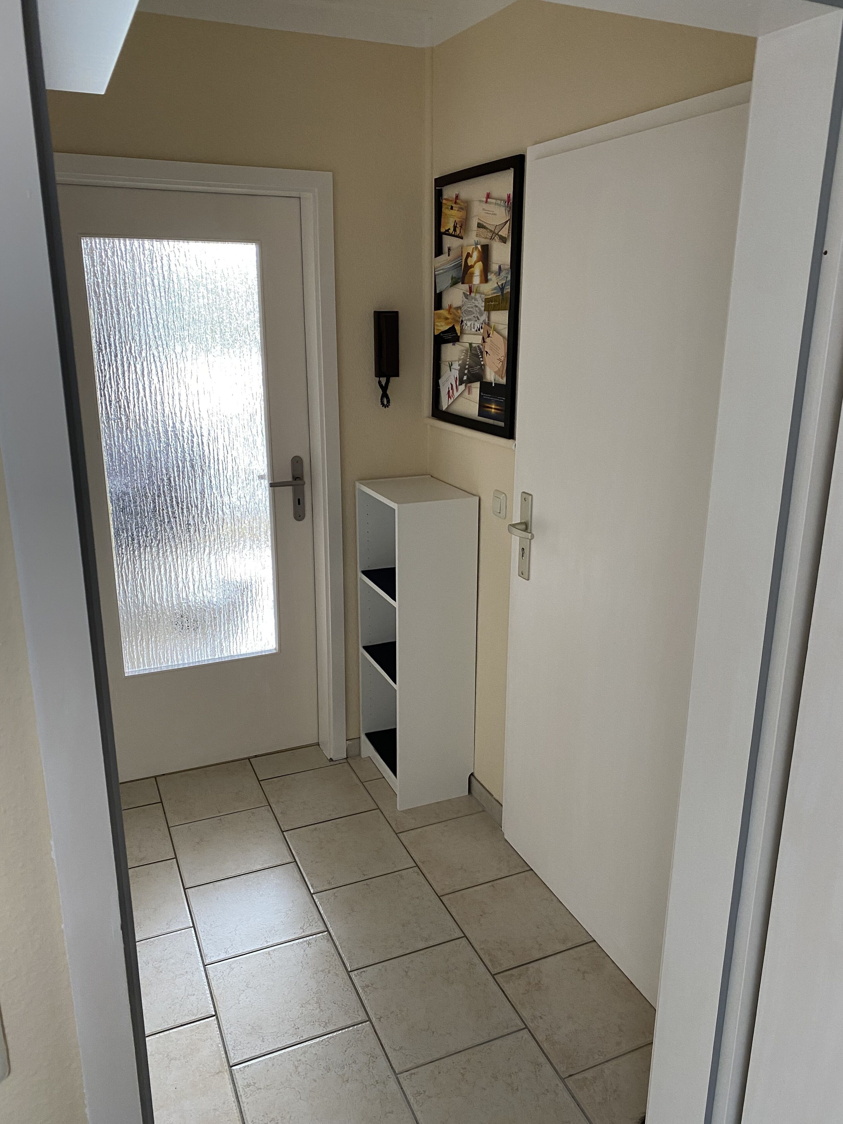 A narrow hallway with a frosted glass door, a white door with a small shelf, and a framed picture on the wall.