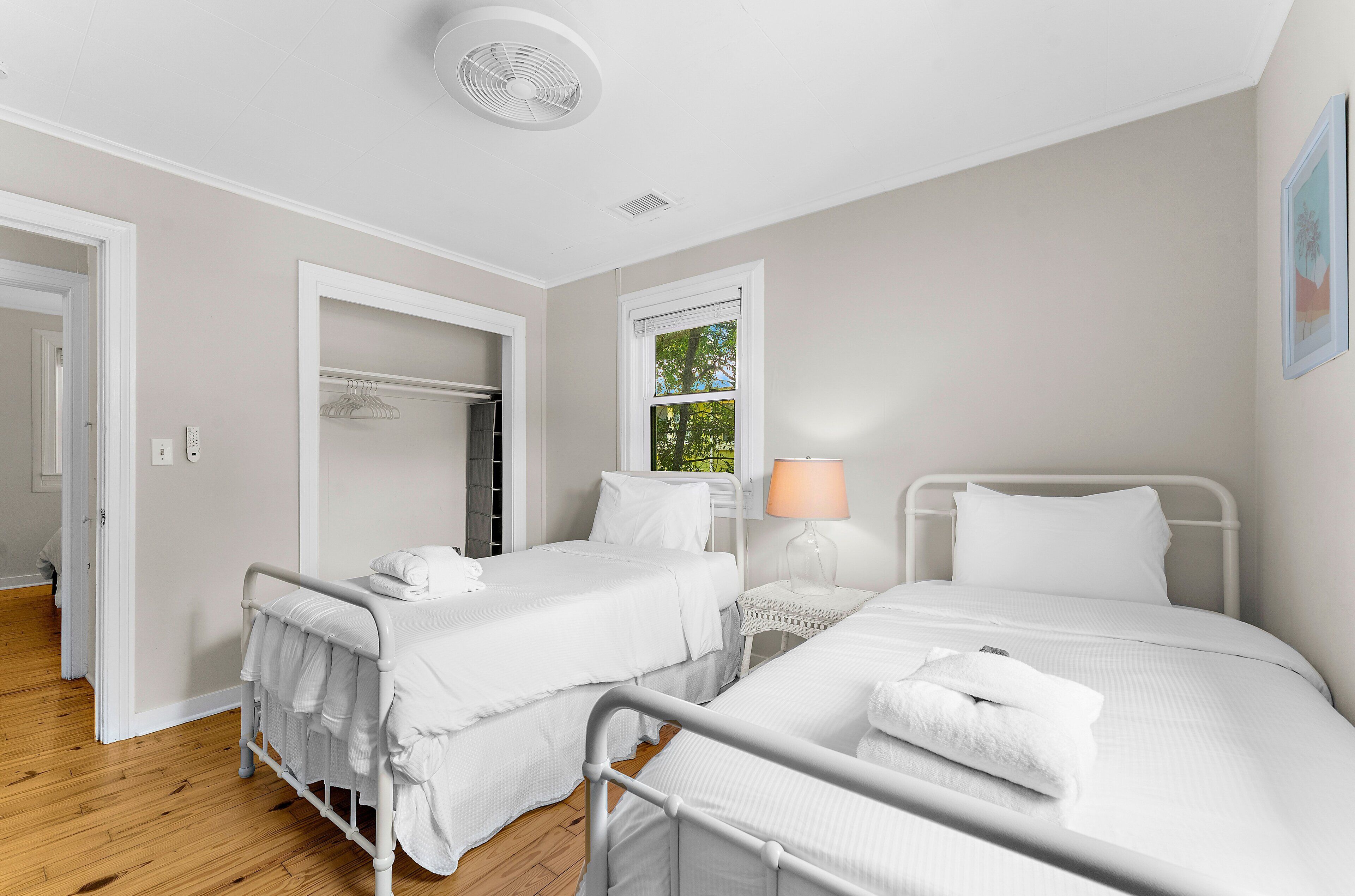 Une chambre d’hôtel avec deux lits, une fenêtre donnant sur un paysage verdoyant, une lampe blanche et un ventilateur de plafond blanc.
