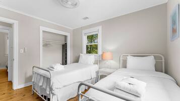 Une chambre d’hôtel avec deux lits, une fenêtre donnant sur un paysage verdoyant, une lampe blanche et un ventilateur de plafond blanc.