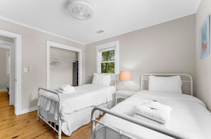 Habitación de hotel con dos camas, una ventana con vistas a zonas verdes, una lámpara blanca y un ventilador de techo blanco.
