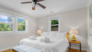 A hotel room with a bed, two bedside tables with lamps, a bench, and a ceiling fan.