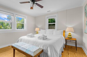 Une chambre d’hôtel comprenant un lit, deux tables de chevet avec des lampes, un banc et un ventilateur de plafond.