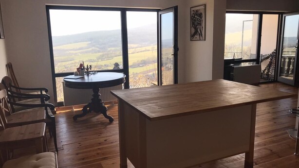 A spacious room with a large wooden table, a round table with a candle holder, and a view of a countryside landscape through large windows. - Panoramic view of the Rhön (Bischofsheim an der Rhön)