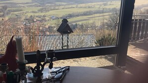 A room with a large window overlooking a rural landscape. Inside, there is a wooden table with a candle holder, glasses, and a decorative item. - Panoramic view of the Rhön (Bischofsheim an der Rhön)