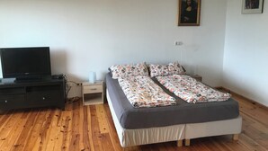 A bedroom with a bed, a TV, a wooden floor, a nightstand, and a hanging light fixture. - Panoramic view of the Rhön (Bischofsheim an der Rhön)