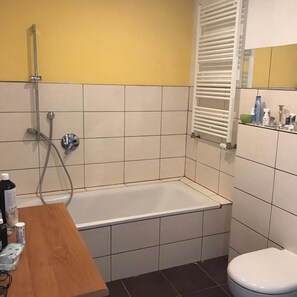 Un baño con bañera, inodoro y un estante con artículos de aseo.