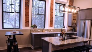 A modern kitchen with granite countertops, a central island with bar stools, and a stainless steel refrigerator. - The Double Diamond Loft (Boyne City)