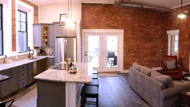 A modern kitchen with granite countertops, a central island, and a dining area with a sofa and chairs. - The Double Diamond Loft (Boyne City)