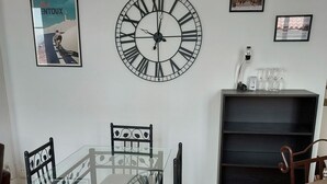 A dining area with a glass table and black chairs, a large wall clock, and framed pictures.