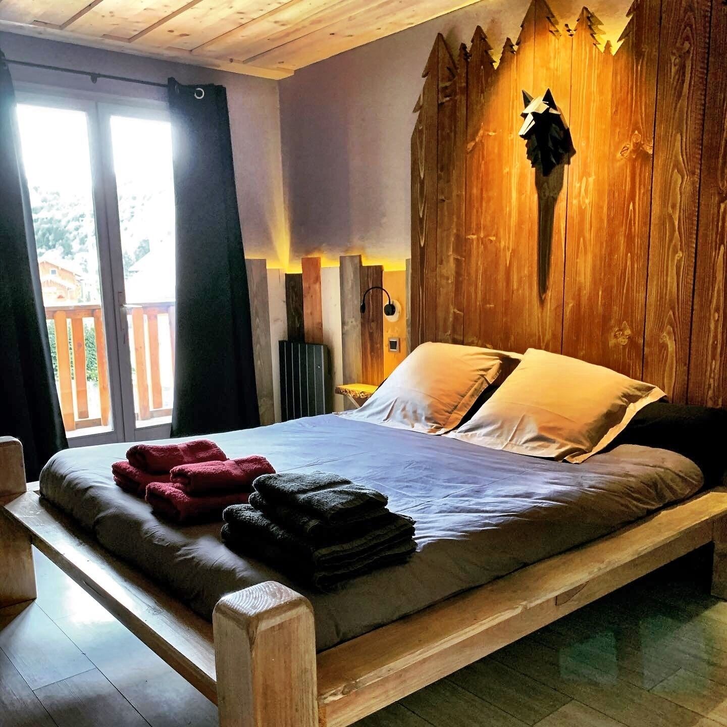 A bedroom with a wooden headboard, a bed with pillows, a bedside table, and a window with curtains.