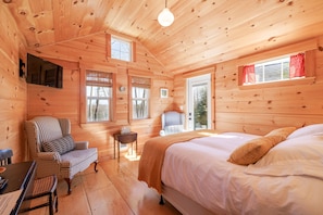 Una baita di legno con un letto, una sedia, un tavolo e un televisore.