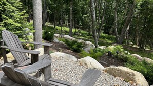 Puinen terassi, jossa on Adirondack-tyylisiä puutarhatuoleja ja kivimurskapolku, ja kaiken ympärillä puita ja kiviä.