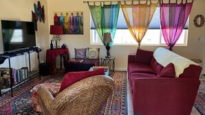 A living room with a television, a sofa, a patterned rug, and a window with colorful curtains. - Pioneertown Bohemian Getaway! (Pioneertown)