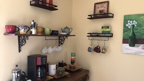 A kitchen with shelves holding various mugs, a coffee maker, and a painting of a bottle. - Pioneertown Bohemian Getaway! (Pioneertown)