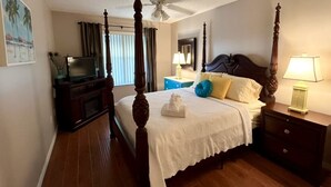 A four-poster bed with a white bedspread, a bedside table with a lamp, and a television on a stand.