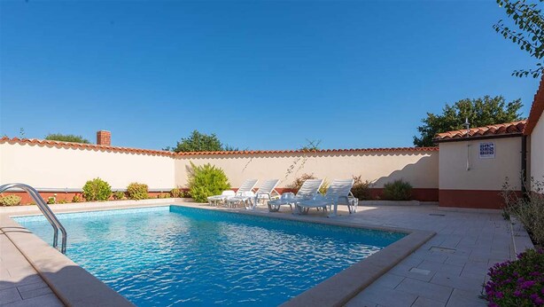 A rectangular swimming pool with a metal ladder on one side, surrounded by white lounge chairs.