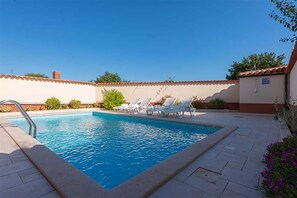 Piscina rectangular con una escalera metálica en un lateral, rodeada de sillas reclinables blancas.