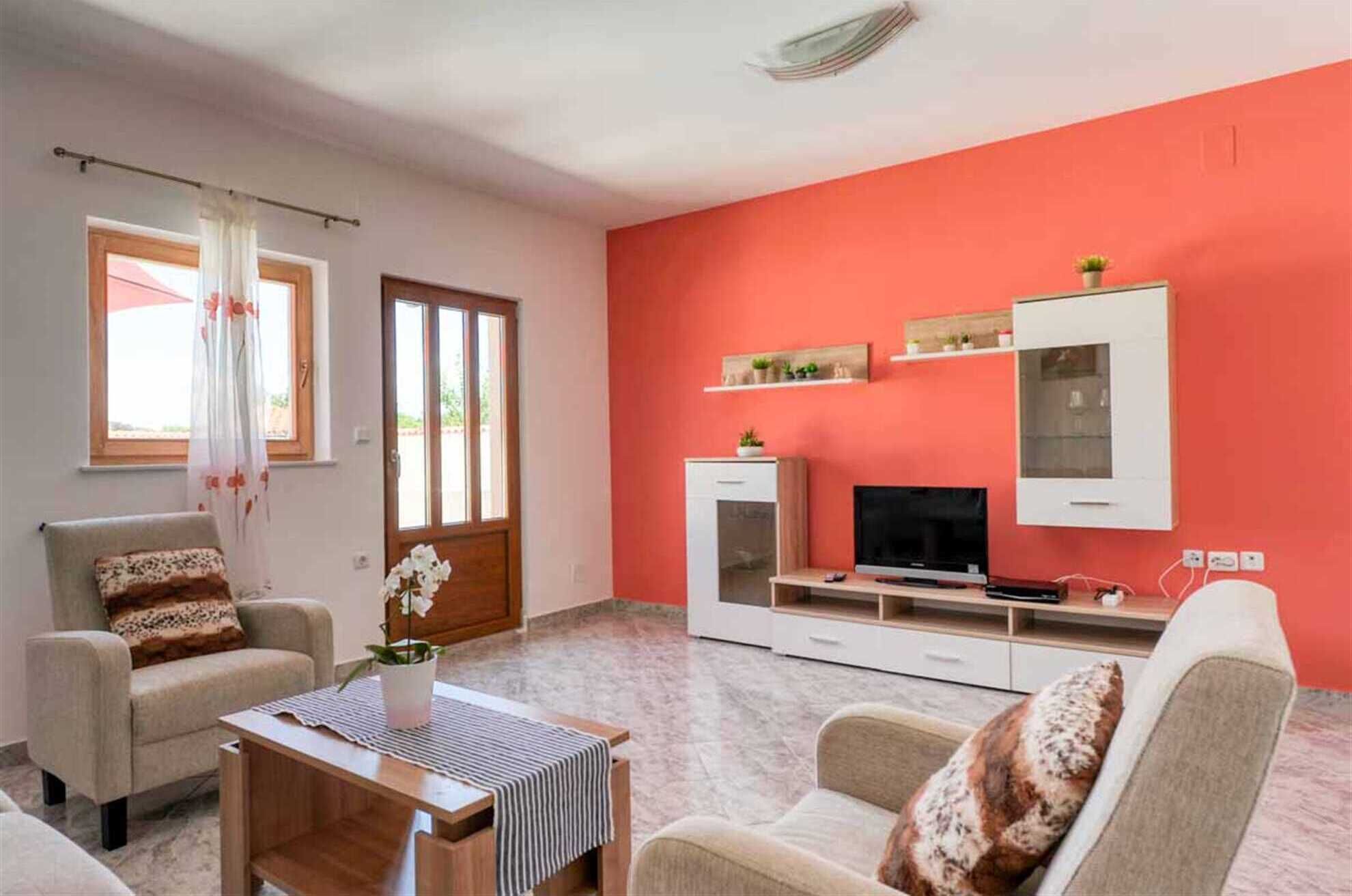 A living room with a red wall, a TV, a cabinet, and a window with curtains.