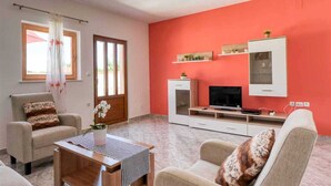 A living room with a red wall, a TV, a cabinet, and a window with curtains.