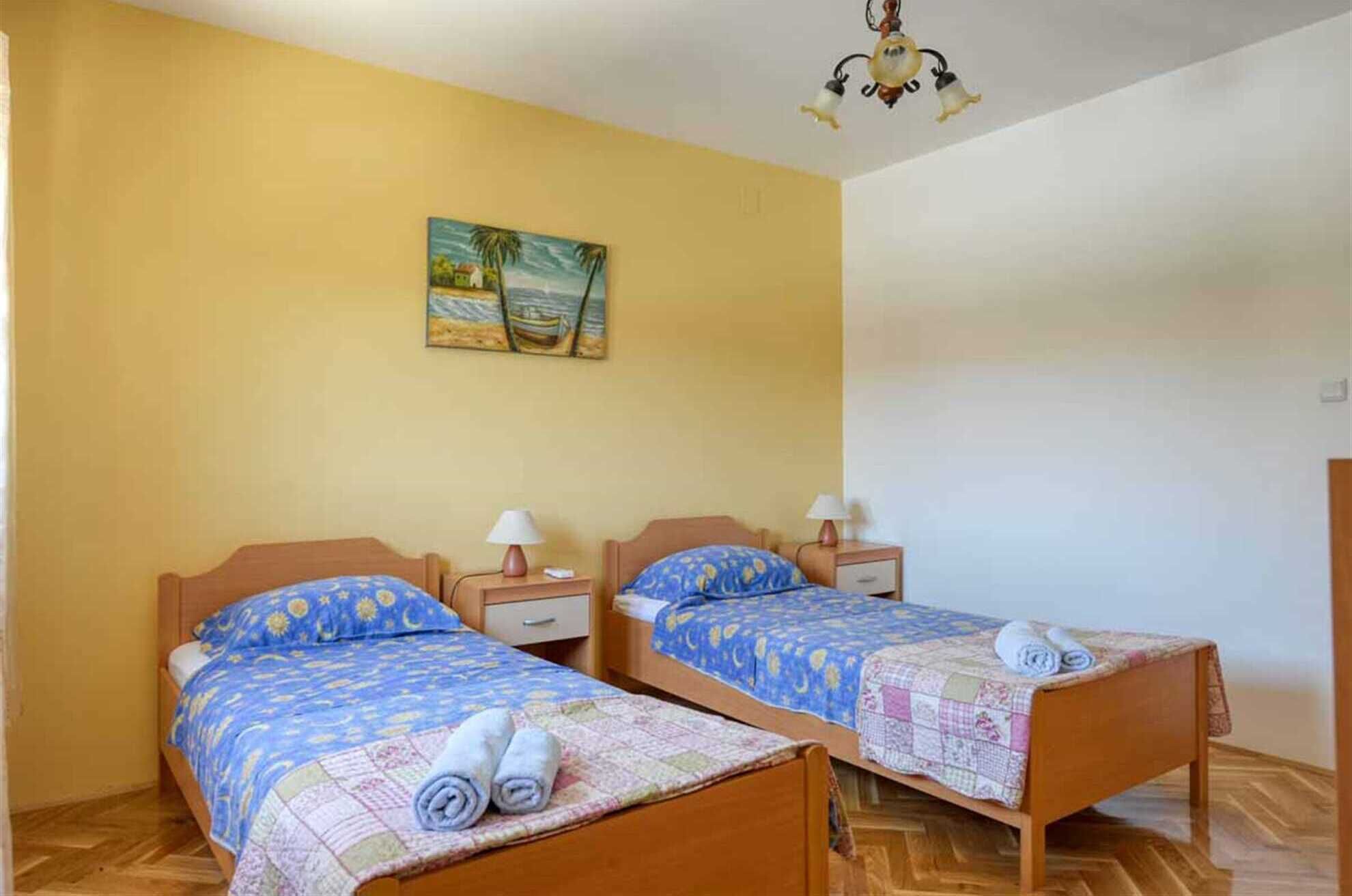 A room with two wooden beds, each with a nightstand and a lamp. There is a painting on the wall above the beds.