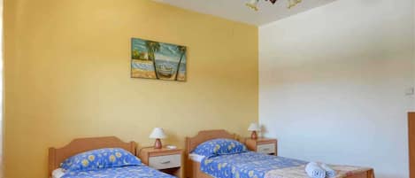 A room with two wooden beds, each with a nightstand and a lamp. There is a painting on the wall above the beds.