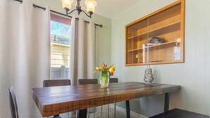 A dining area with a wooden table, chairs, a vase with flowers, and a shelf with decorative items.