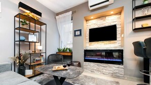 Una sala de estar moderna con chimenea de piedra, un televisor de pantalla plana, un sofá cómodo y una mesa de centro con una copa de vino.