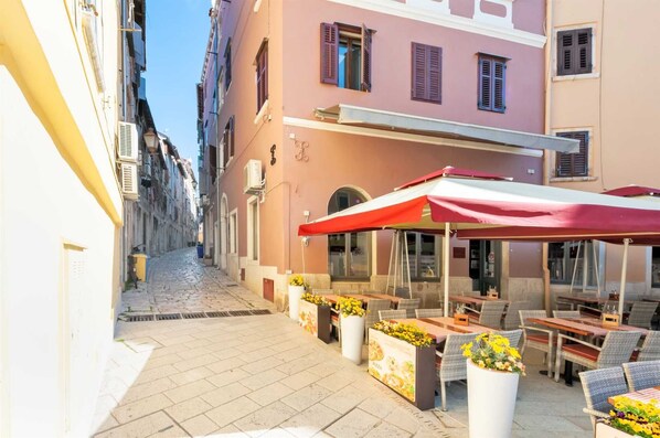 A narrow street with a row of outdoor seating areas, each with a red canopy and potted plants.