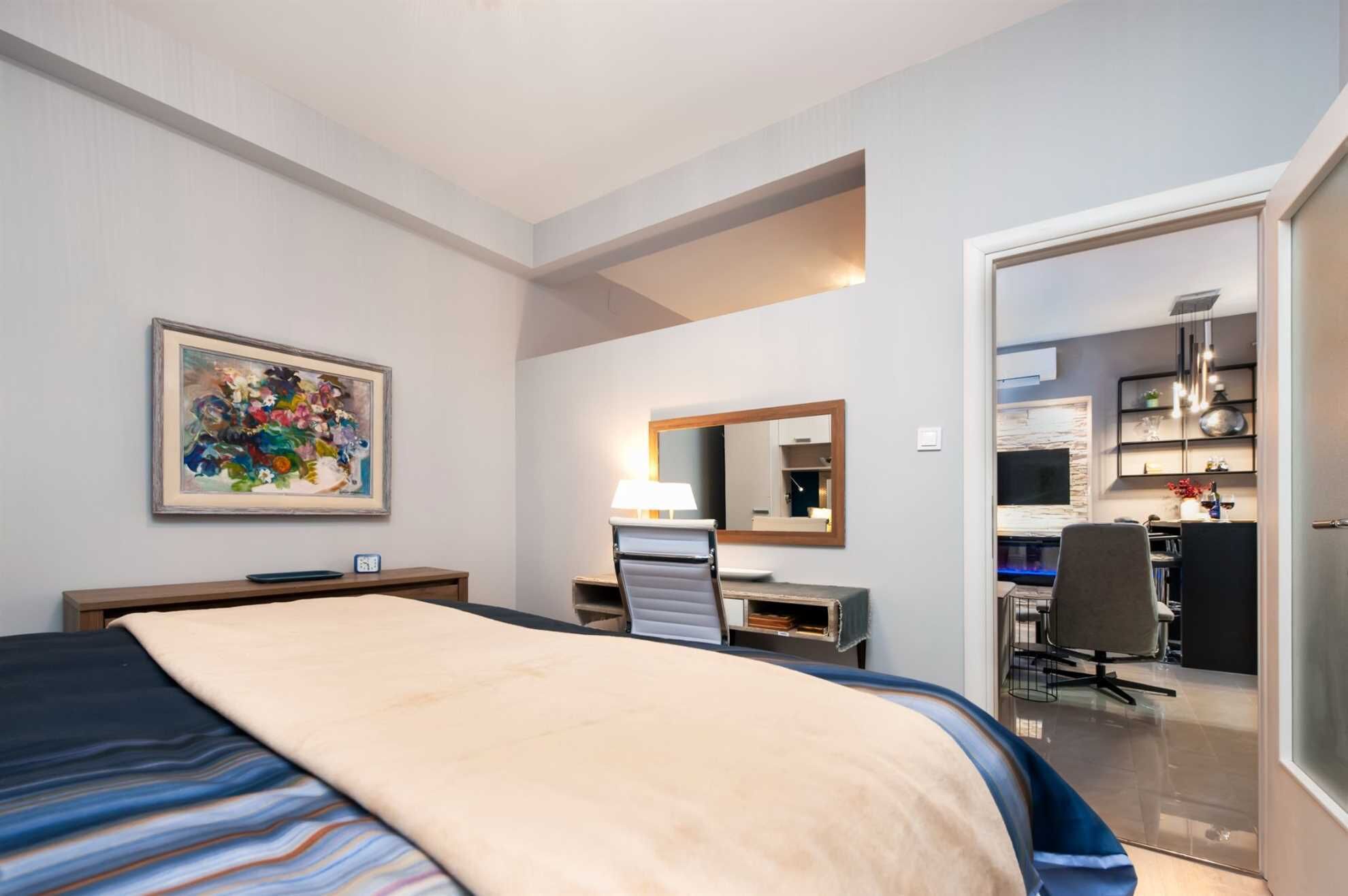 A hotel room with a bed, desk, chair, and a large mirror.