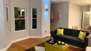 A modern living room with a dark grey sofa, yellow cushions, and a yellow ottoman with decorative items. - MODERN MASSIVE LARGE GROUP 3800sf MIT HARVARD BOS (Somerville)