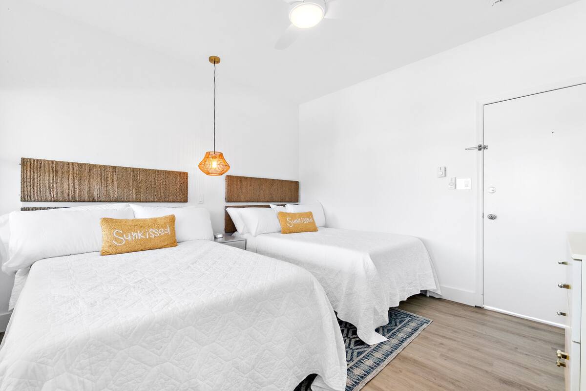 Habitación de hotel con dos camas, un cabecero de madera, una lámpara colgante y una puerta.