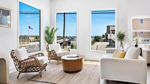 A spacious living room with large windows, wicker furniture, and a view of the street. - The Hideaway Hotel (Beach Haven)
