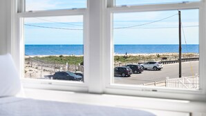 A room with a large window overlooking a beach and parking area. - The Hideaway Hotel (Beach Haven)