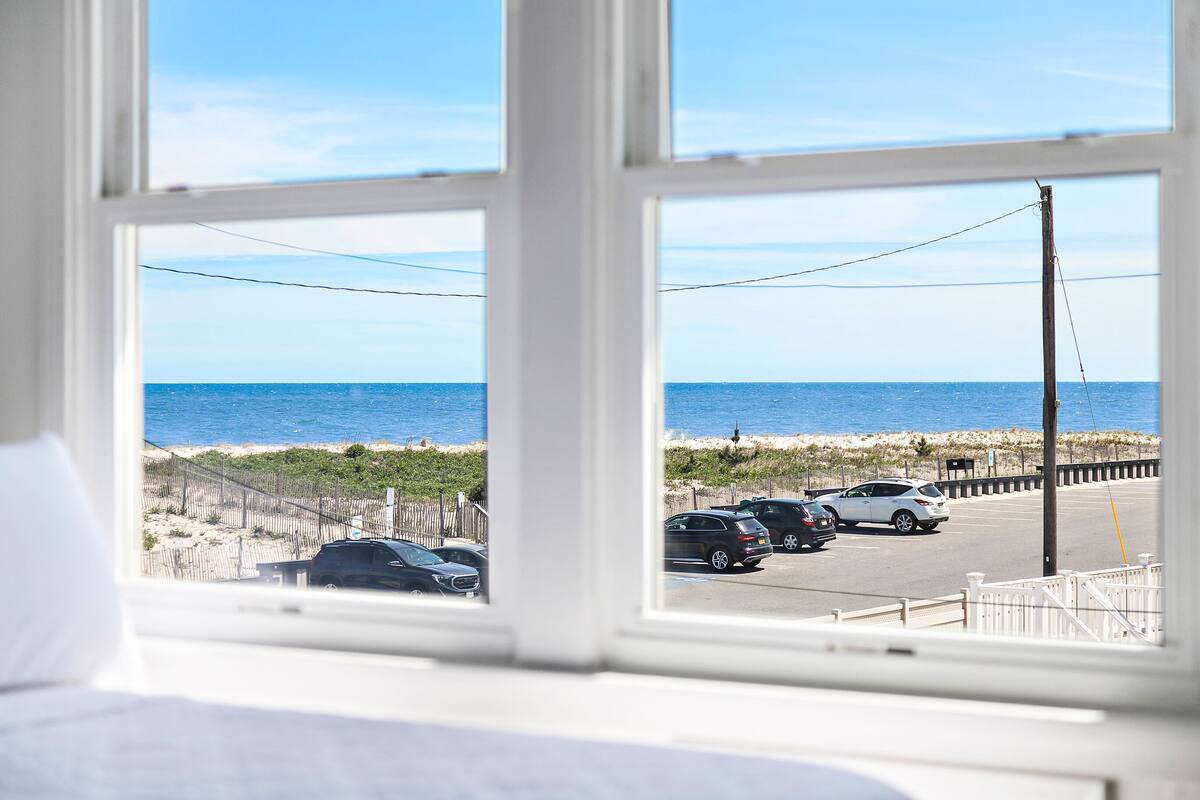 Una habitación con un amplio ventanal con vista a una playa y un estacionamiento.