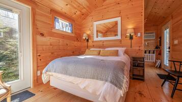Une chambre à coucher dans une cabane en bois, avec un lit, deux lampes de chevet, un miroir, une petite étagère et une fenêtre.